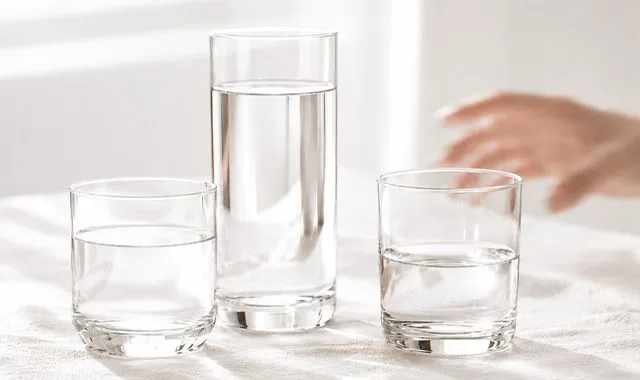 Tres vasos de agua fresca de distintos tamaños sobre una mesa luminosa